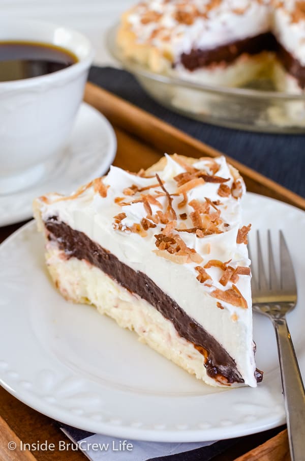 A white plate with a slice of coconut cream chocolate pudding pie topped with Cool Whip and toasted coconut and more pie behind it