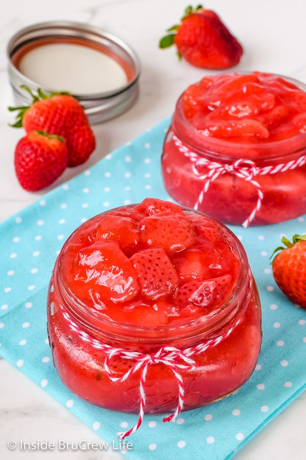 An overhead picture of two clear jars on a blue towel filled with homemade strawberry pie filling.