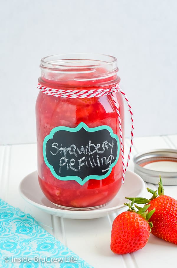 A large canning jar on a white plate filled with homemade strawberry pie filling.
