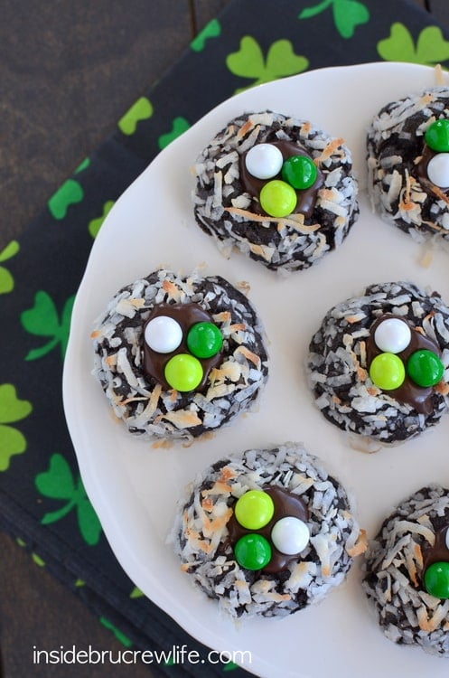 Chocolate cookies on a white plate with green candies on them.