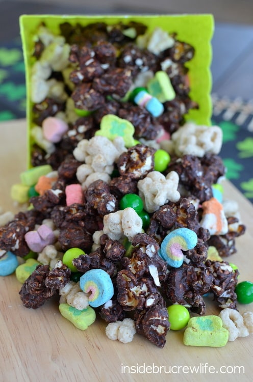 Chocolate popcorn mixed with Lucky Charms spilled out onto a table from a square popcorn container.