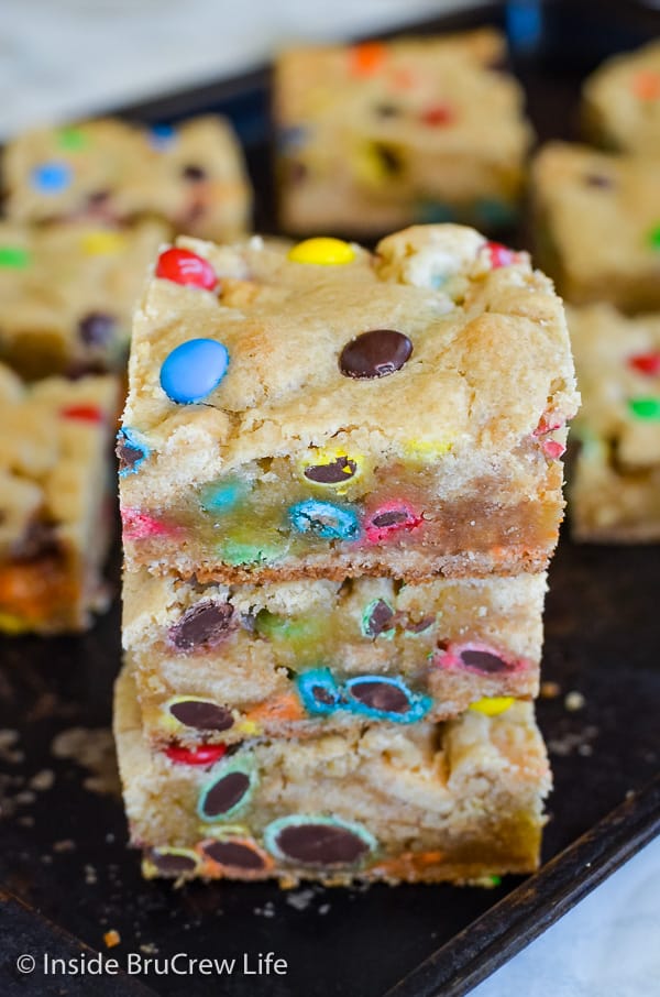 Three M&M Blonde Brownies stacked on top of each other on a dark tray