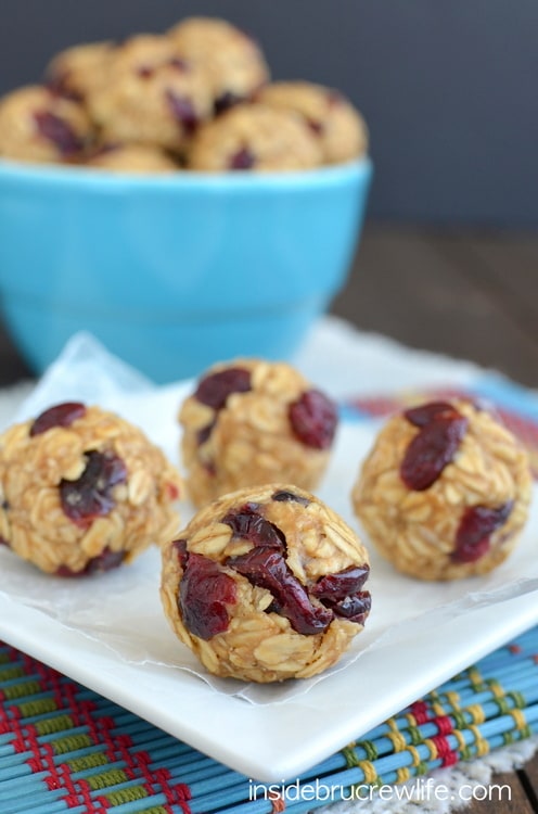 Four peanut butter cranberry granola bites on a white plate with a blue bowl full of bites behind it