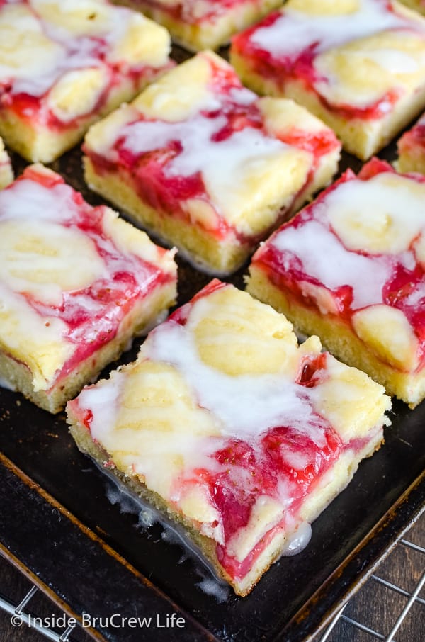 Close up picture of squares of strawberry lemon cake drizzled with glaze on a dark cookie sheet