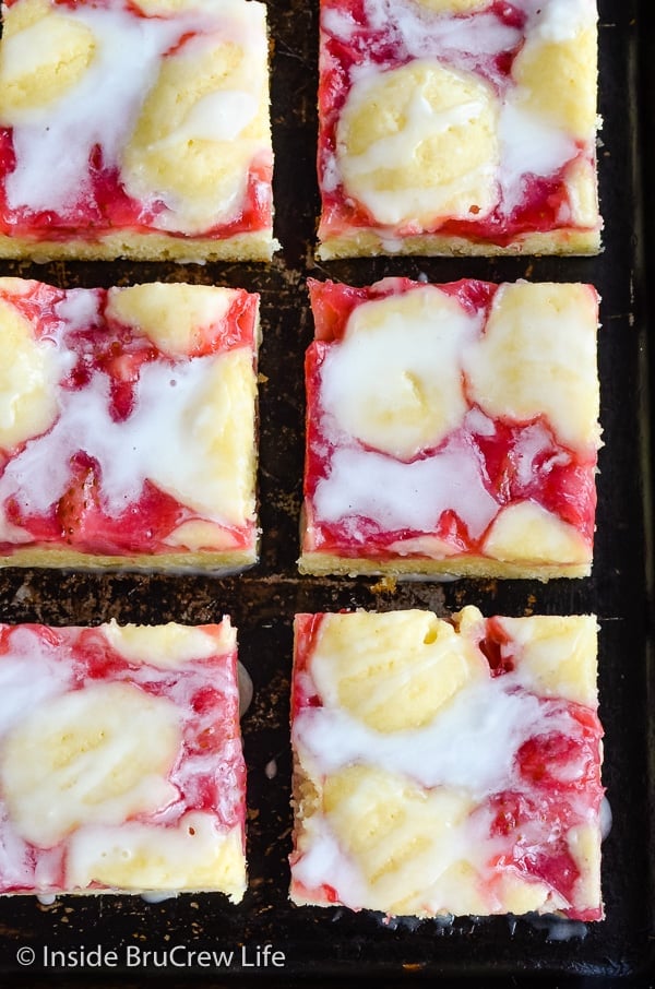 Overhead picture of squares of strawberry lemon snack cake drizzled with glaze on a dark cookie sheet