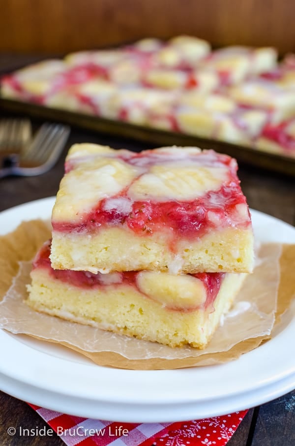 Two white plates with two squares of strawberry lemon cake stacked on top of them