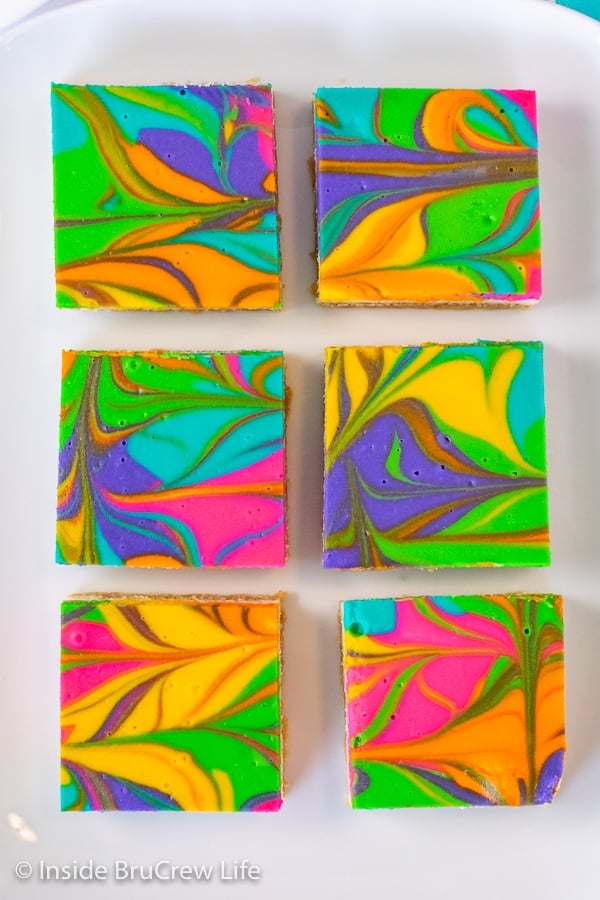 Overhead picture of six rainbow cheesecake bars on a white tray.