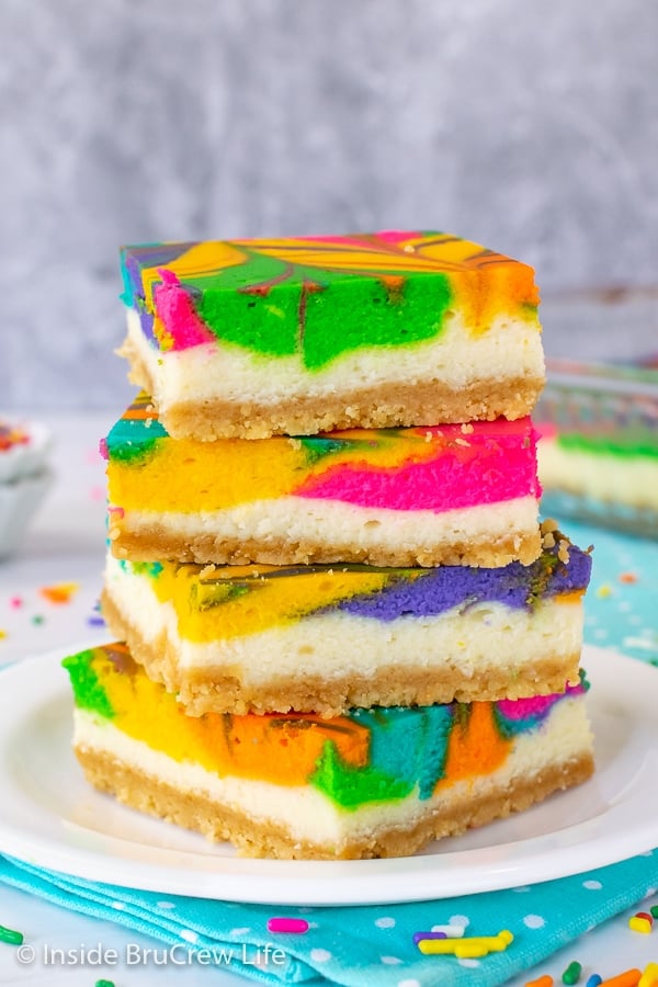 Four rainbow cheesecake bars stacked on top of each other on a white plate