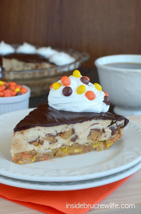 A white plate with a slice of triple peanut butter cookie pie topped with whipped cream and Reese's pieces