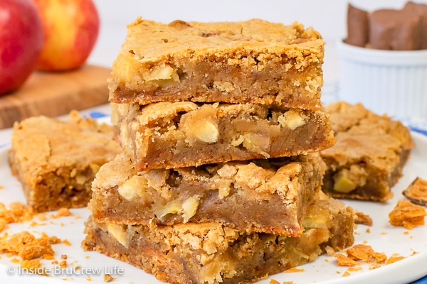 A white plate with four butterfinger apple blondies stacked on it and crushed candy bars around it.