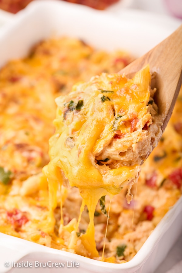 A wooden spoon lifting out cheesy pasta from a white casserole pan.