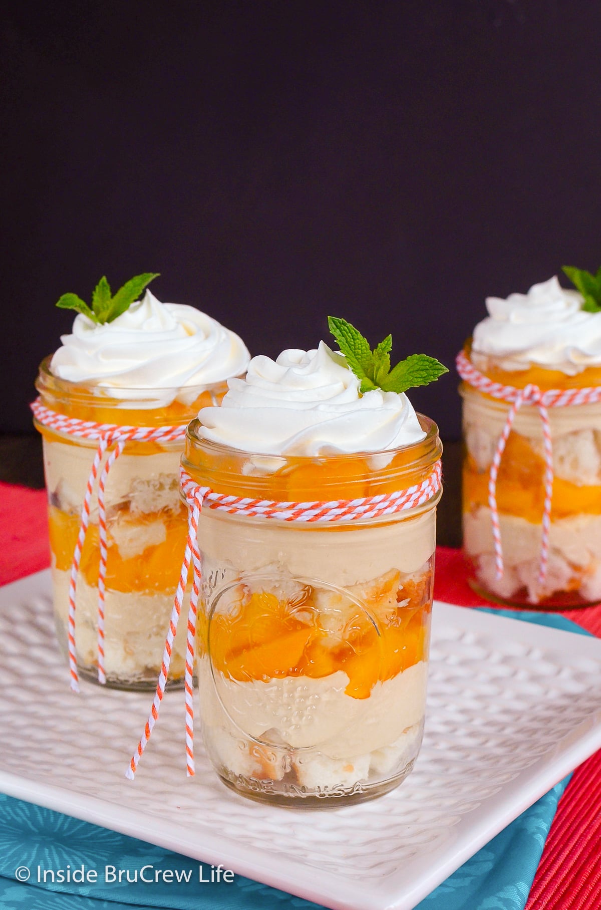 Three jars filled with layers of cake, cheesecake, peaches, and Cool Whip.