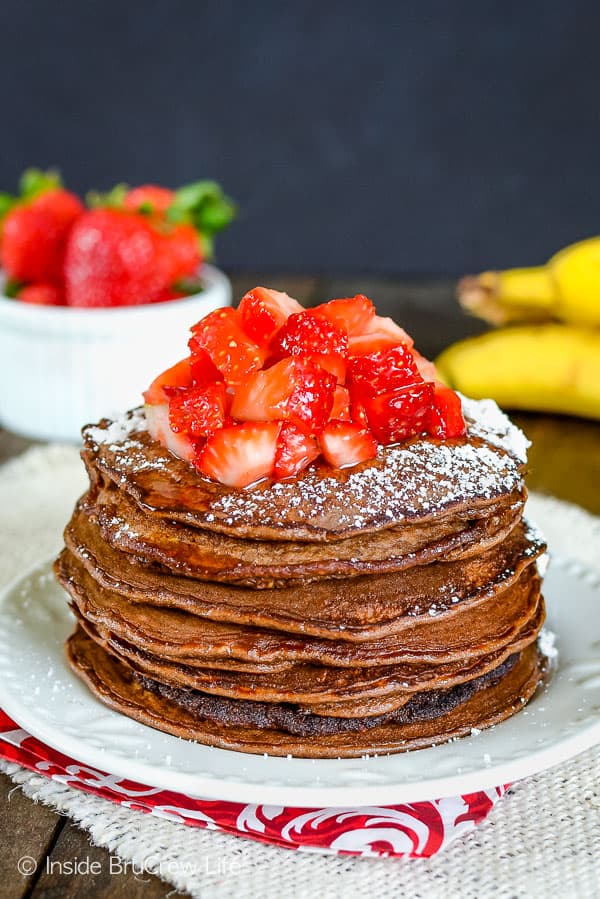 A white plate with a stack of chocolate pancakes with strawberries on it.