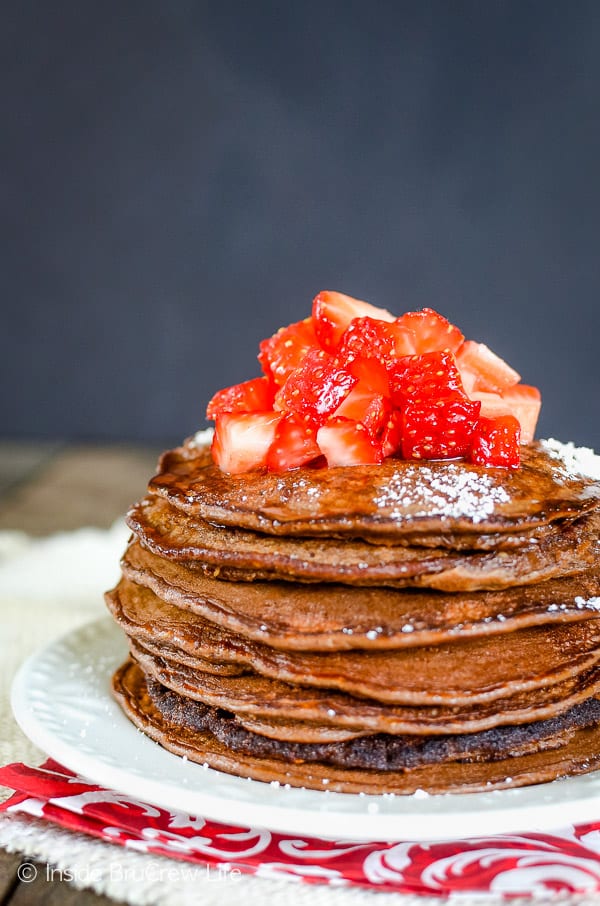 A white plate with a stack of chocolate pancakes on it.