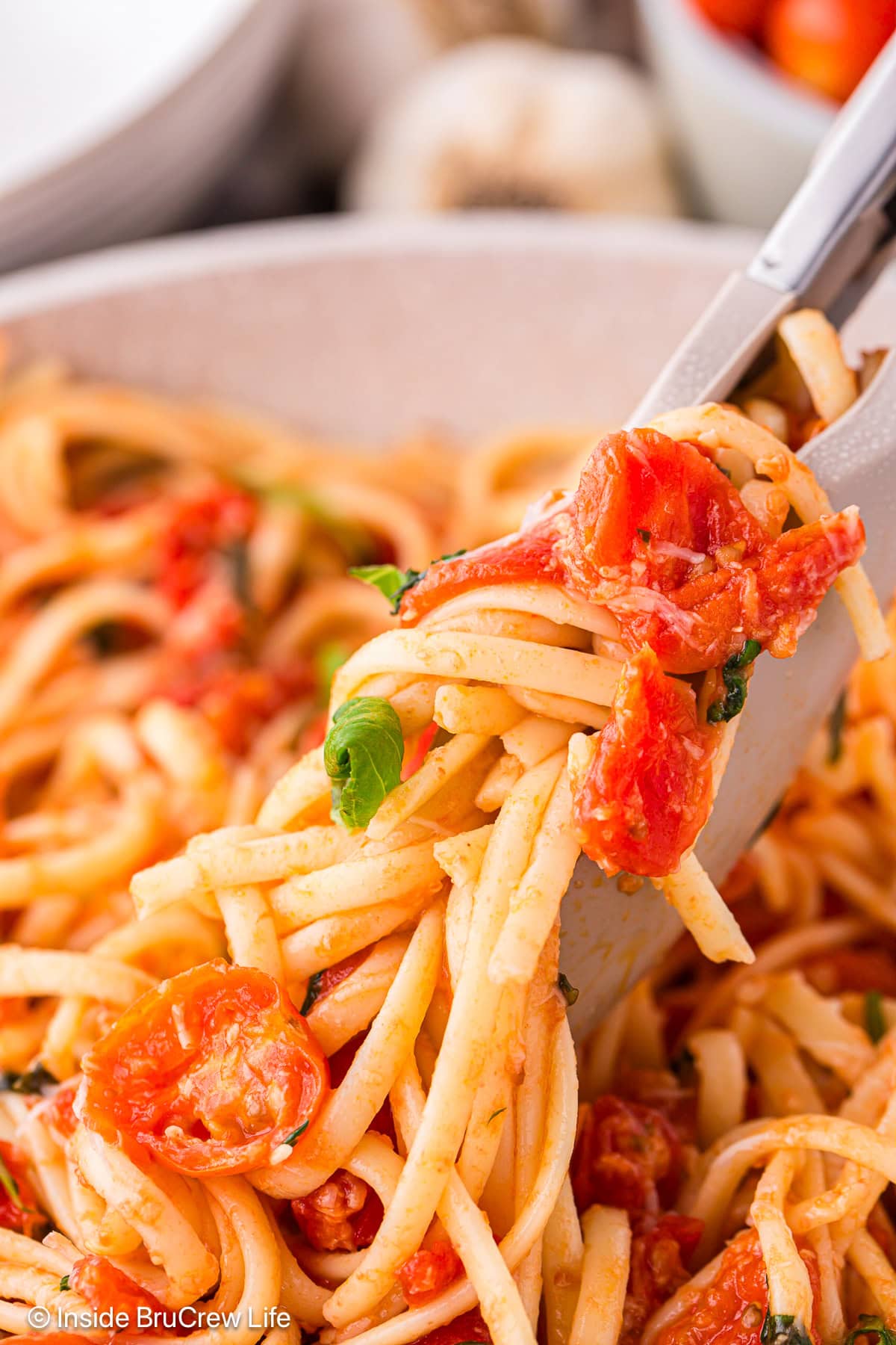 Tongs lifting tomato pasta out of a skillet.