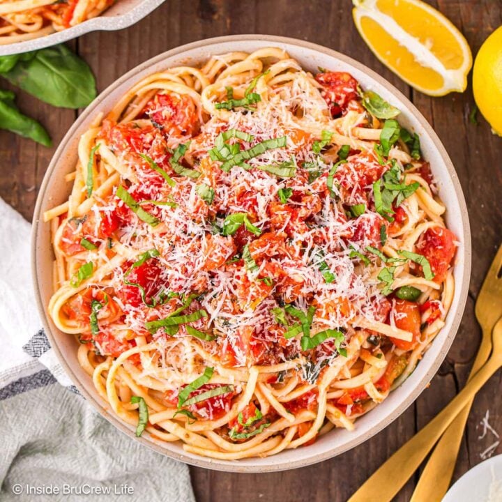 A bowl of tomato basil pasta topped with cheese and fresh herbs.