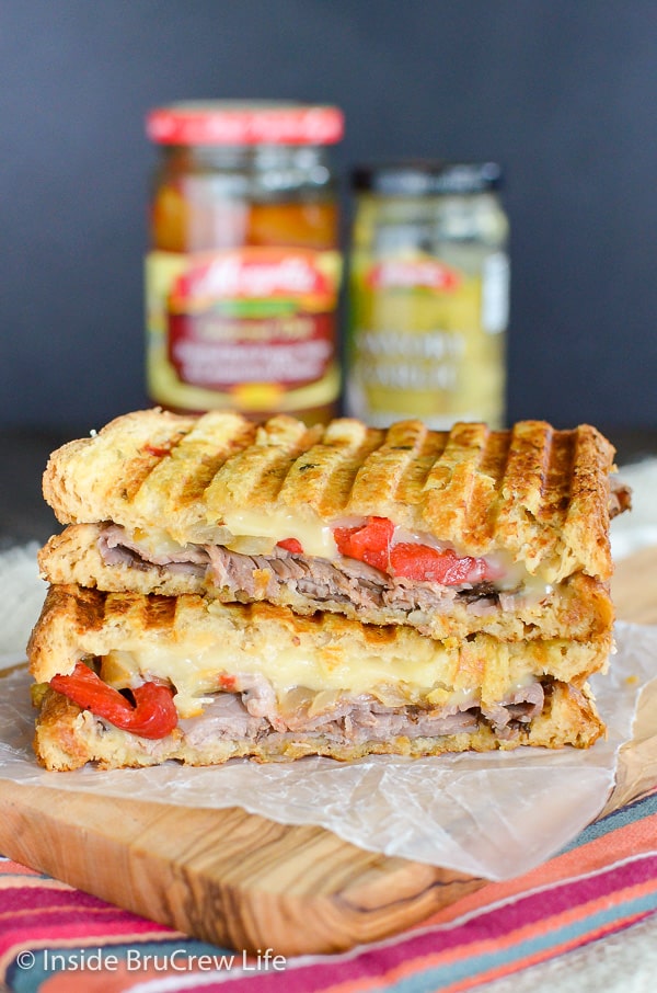 Two halves of Cheesy Beef Panini stacked on top of each other with jars of ingredients behind it
