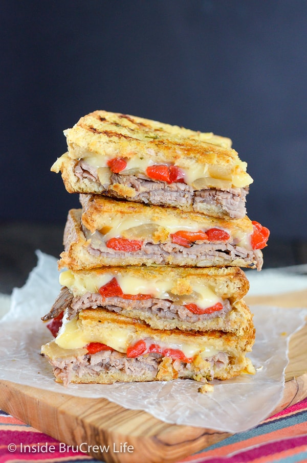 Four squares of Cheesy Beef Panini sandwiches stacked on top of each other on a cutting board