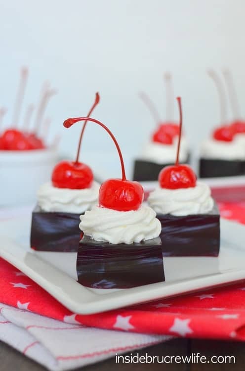 Squares of Jello jigglers on a plate with cool whip and cherries.