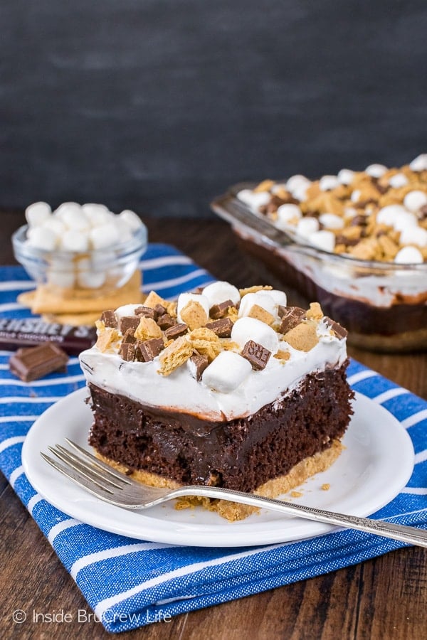 A white plate on a blue towel with a square of chocolate s'mores pudding cake and a fork on it