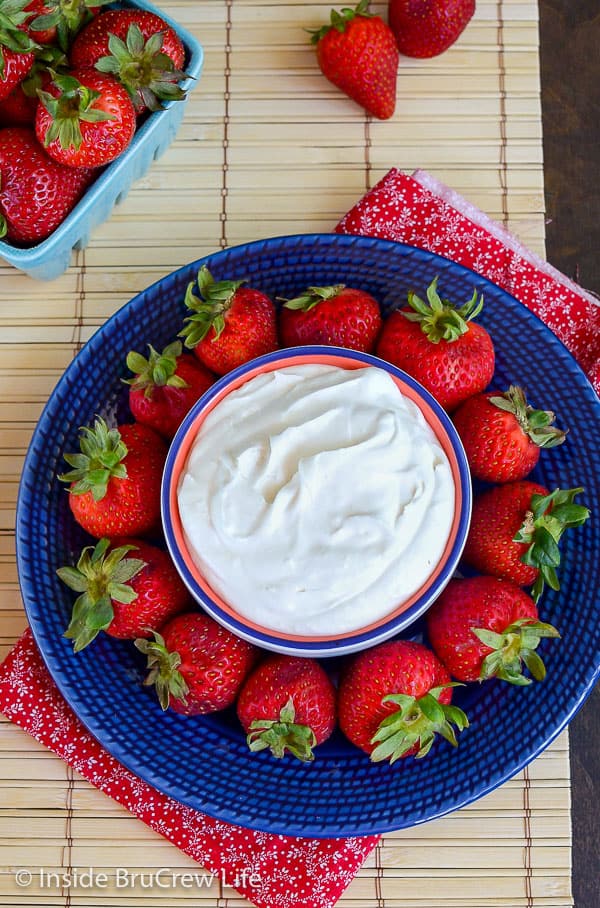 Overhead picture of a blue plate with strawberries and a bowl of coconut cream fruit dip on it