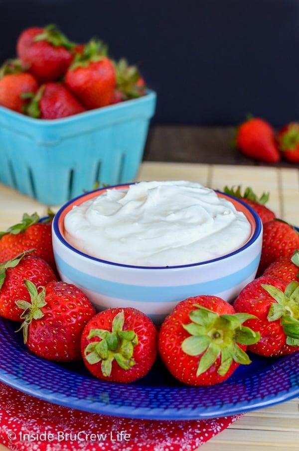A blue plate with strawberries and a bowl of coconut cream fruit dip on it
