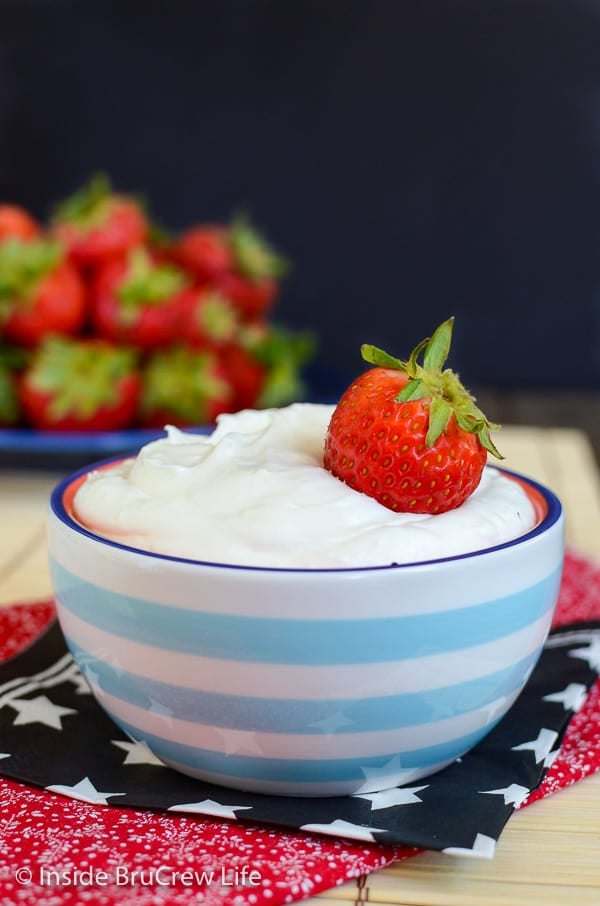 A blue and white bowl filled with coconut cream fruit dip and a plate of strawberries behind it