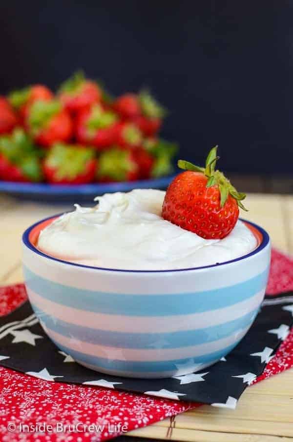 A blue and white bowl filled with coconut cream fruit dip and a strawberry on top