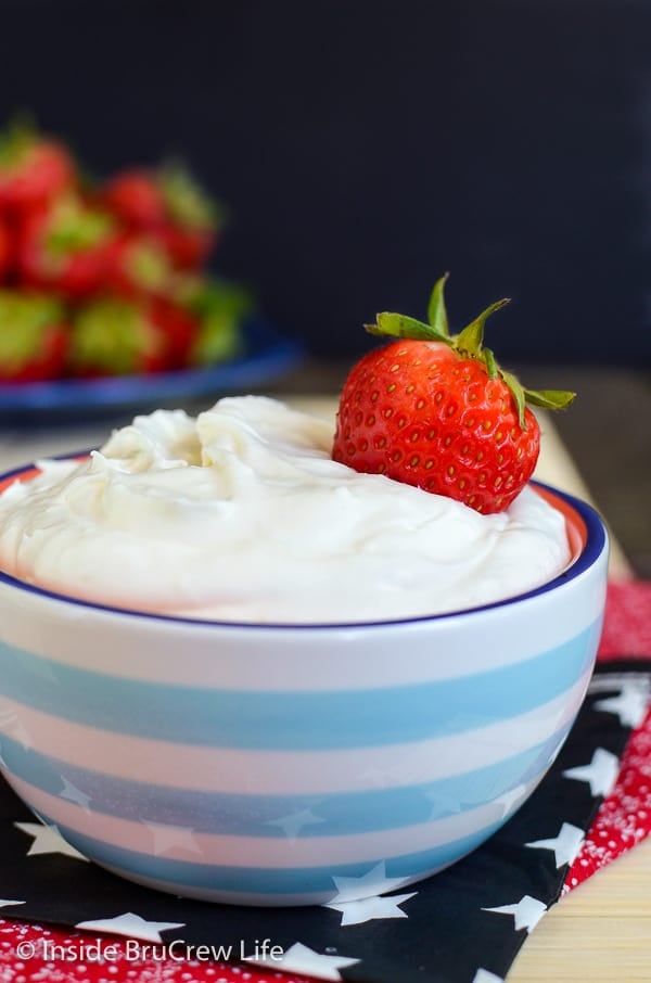 Close up of a blue and white bowl filled with coconut cream fruit dip and a strawberry