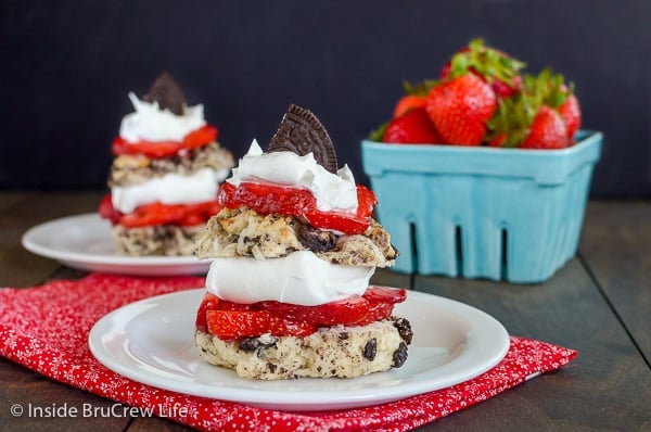 Two white plates on a red towel with layers of Coconut Oreo Strawberry Shortcakes, whipped cream, and fresh strawberry slices