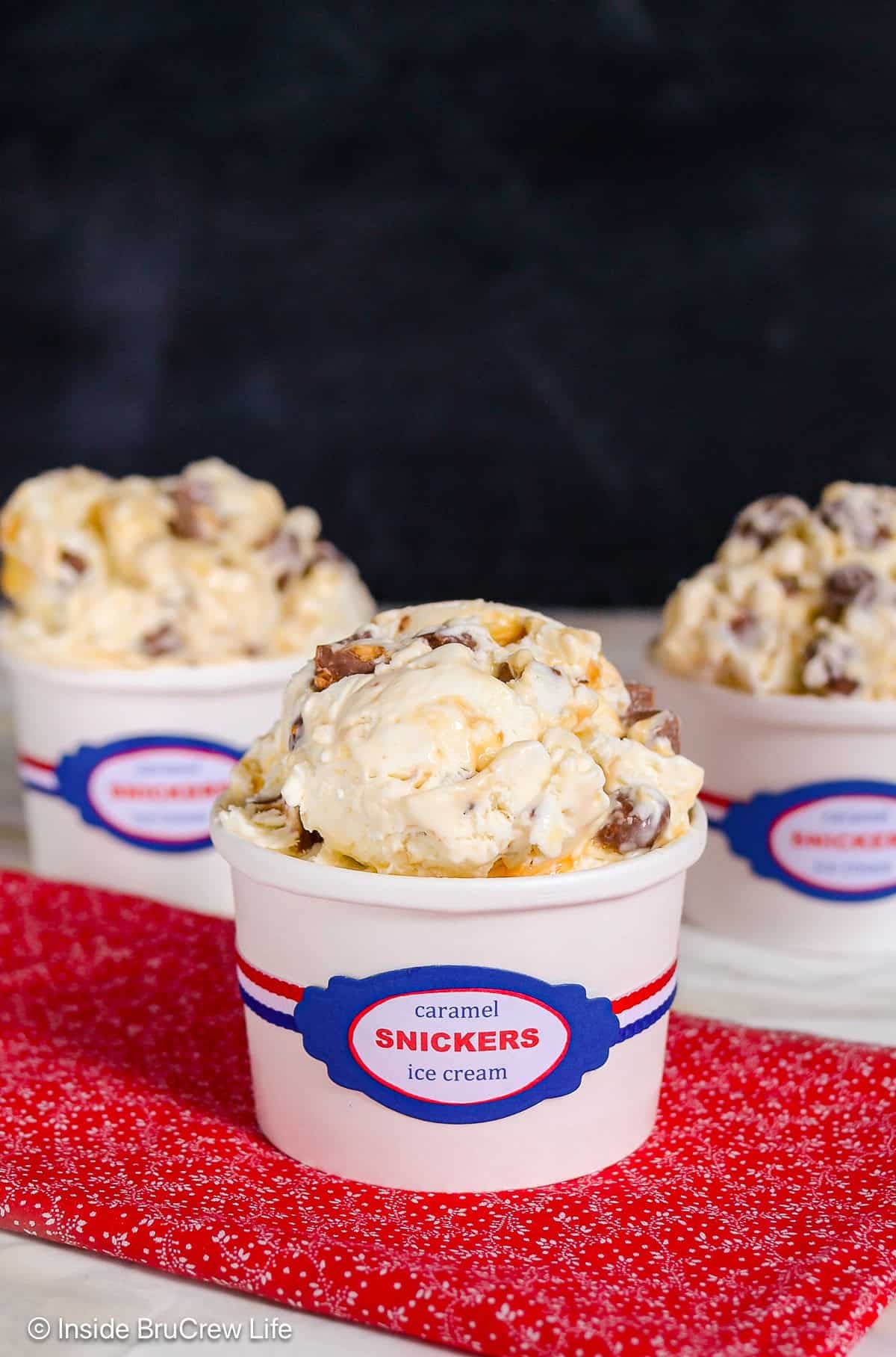 Three small white containers filled with no churn Snickers ice cream scoops.