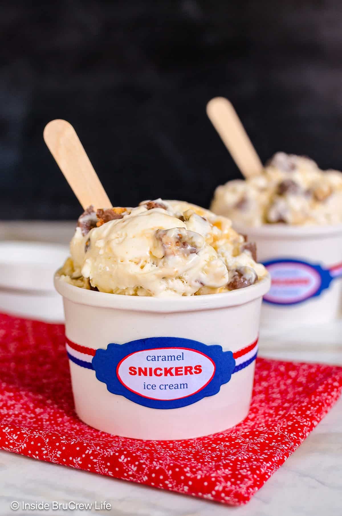 Two white containers filled with homemade Snickers ice cream and wooden spoons.