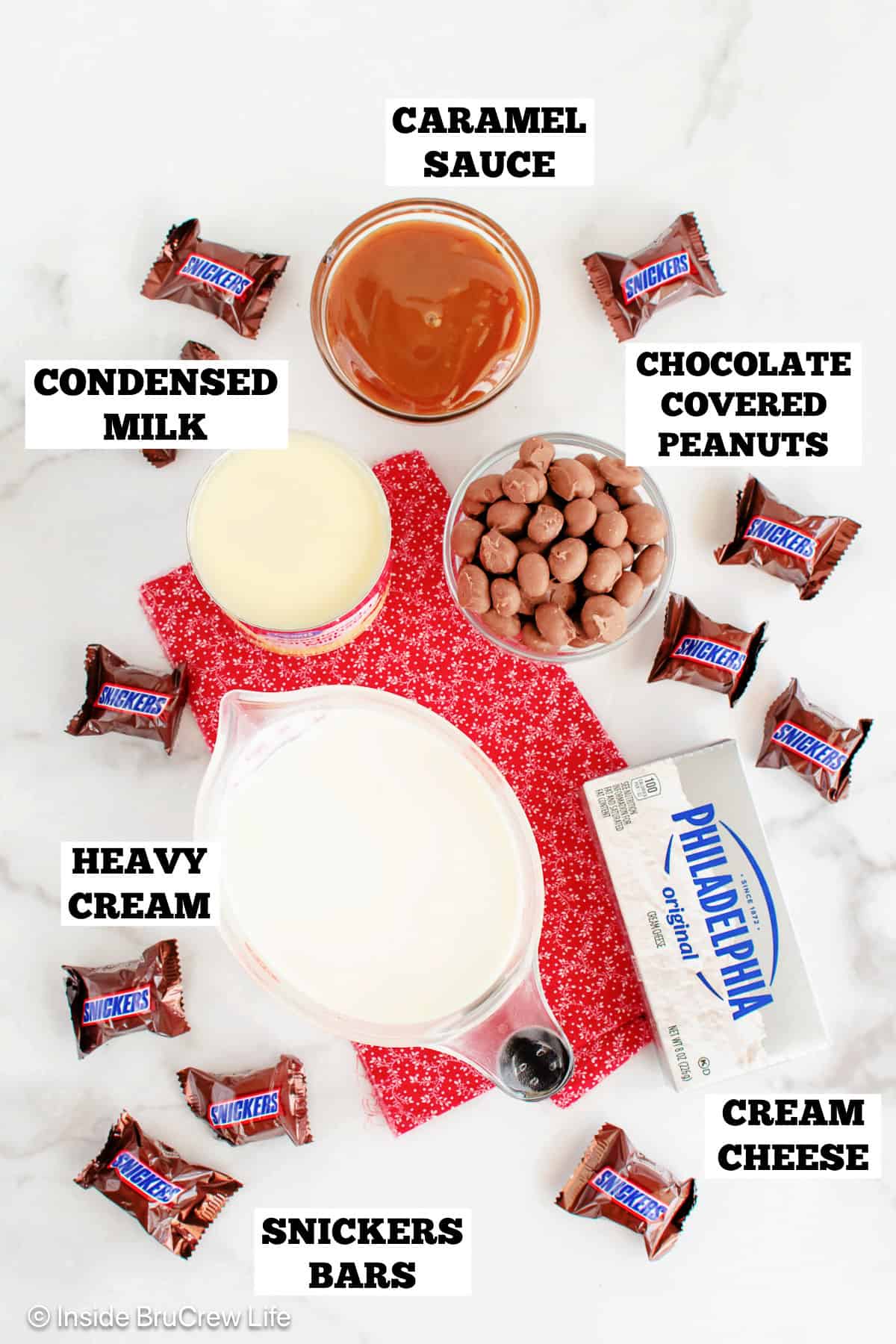 Ingredients for a no churn Snickers ice cream recipe on a white board with labels.