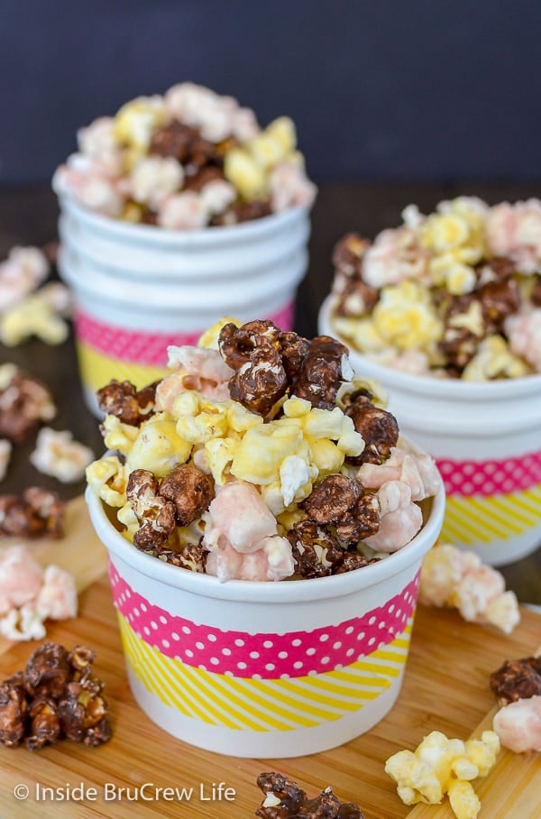 A white bowl overflowing with chocolate, strawberry, and banana popcorn and more filled bowls in the background