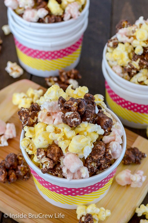 Overhead picture of a white bowl on a wood board filled with chocolate, strawberry, and banana popcorn