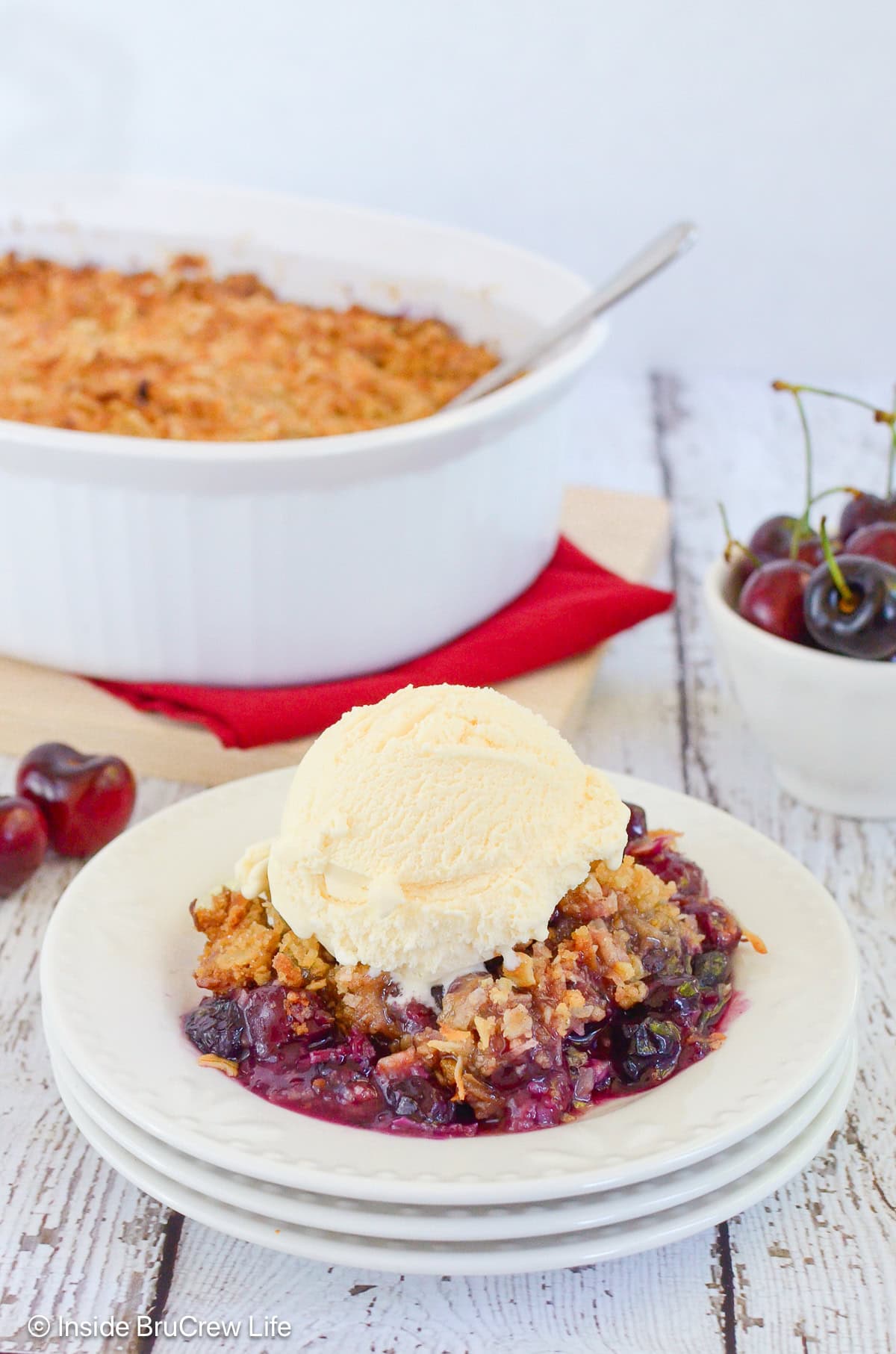 Cherry berry crisp in a bowl topped with vanilla ice cream.