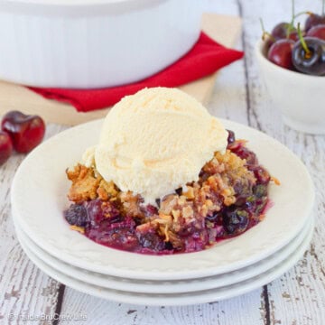 Cherry berry crisp in a bowl topped with vanilla ice cream.