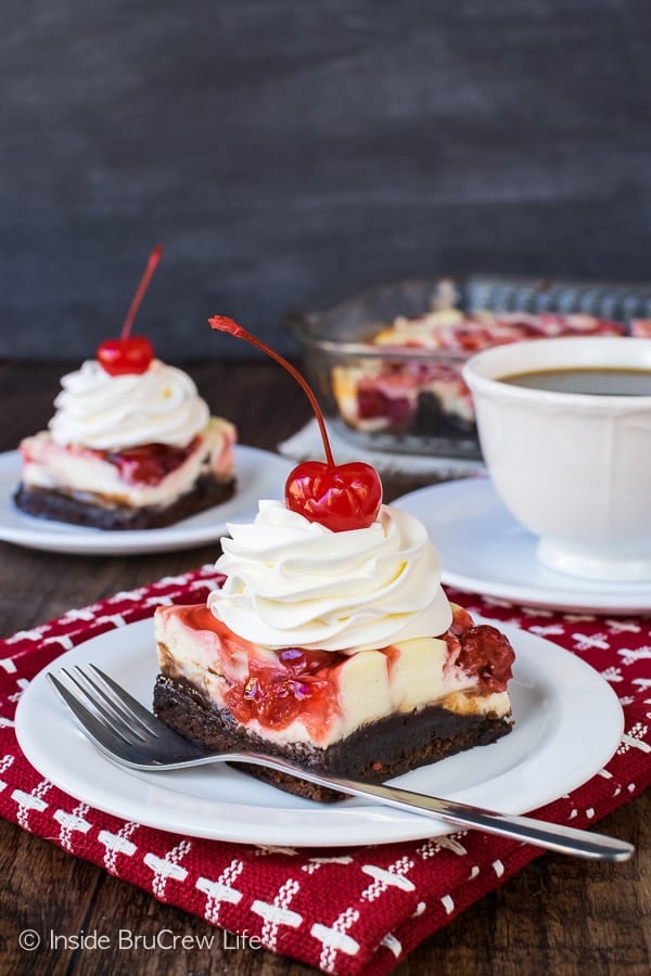 Two white plates on a red towel with squares of cherry cheesecake brownies and forks on them