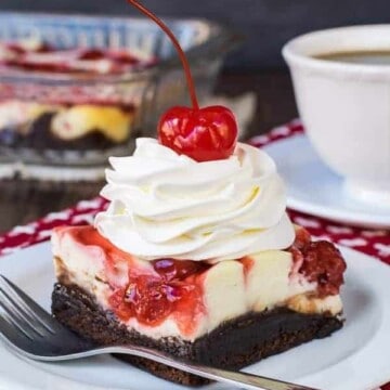 A white plate with a square of cherry cheesecake brownies topped with cool whip and a cherry