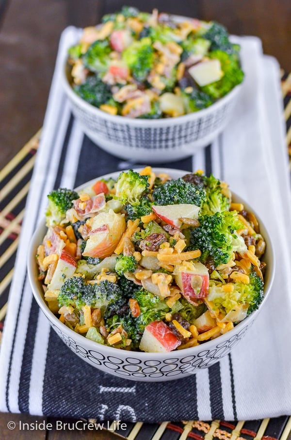Two white bowls on a black and white towel filled with broccoli salad