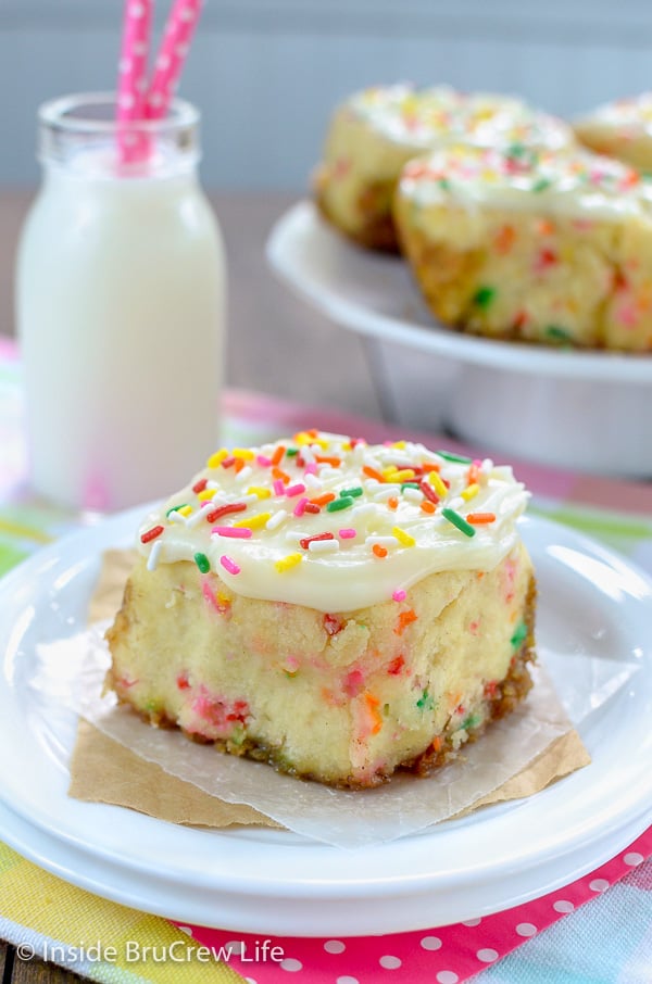 A Funfetti Cinnamon Roll with frosting and sprinkles on top on a white plate with a glass of milk behind it