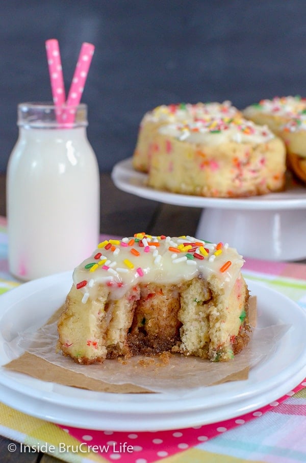 Half of a funfetti cinnamon roll with glaze and sprinkles on a white plate showing the gooey cinnamon filling inside