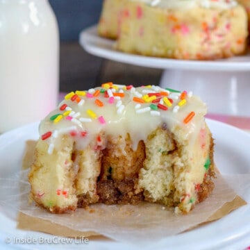 A white plate with a funfetti cinnamon roll topped with glaze and sprinkles with a bite taken out of it