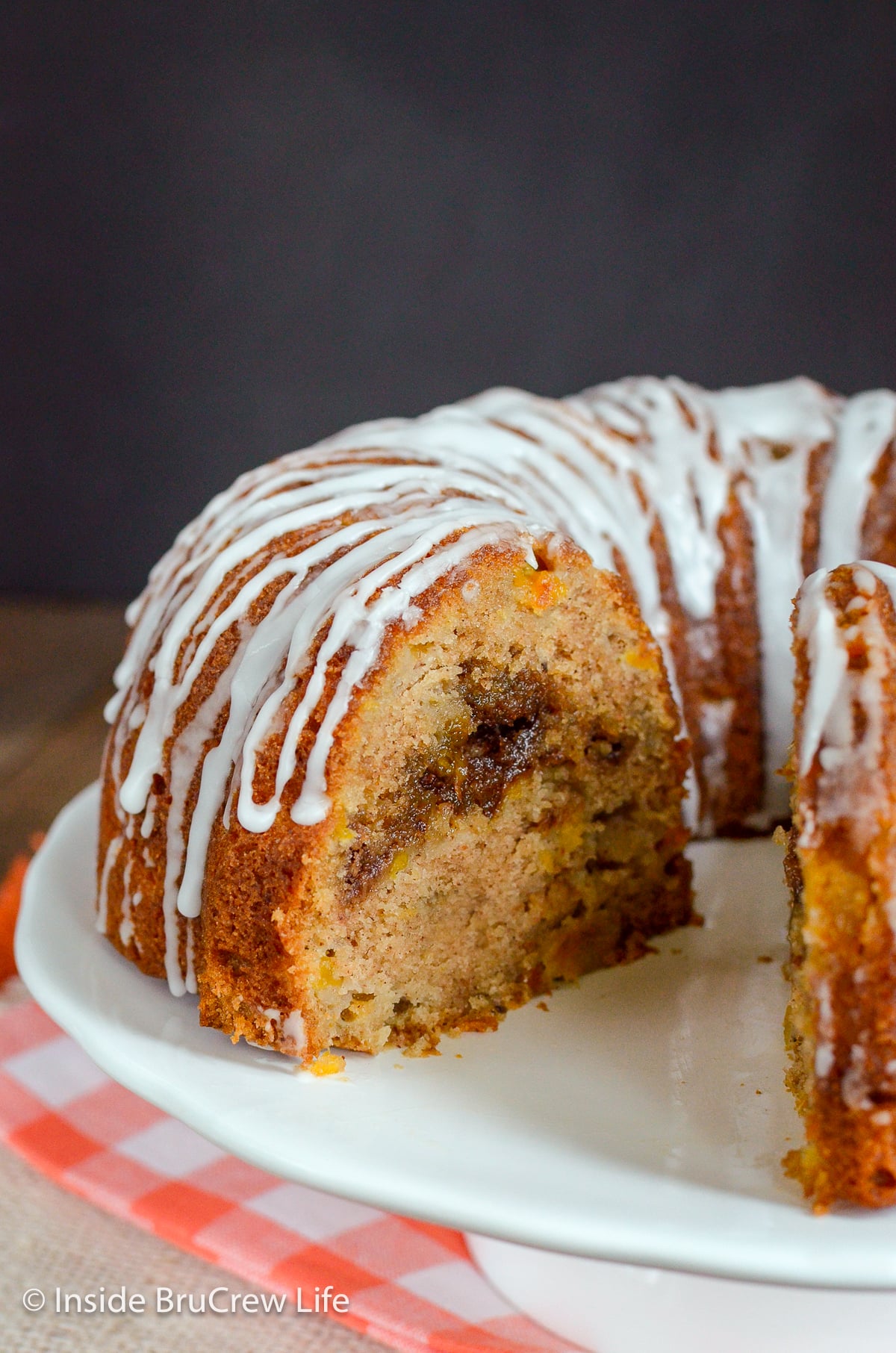 A white cake plate with a full bundt cake topped with white glaze on it.