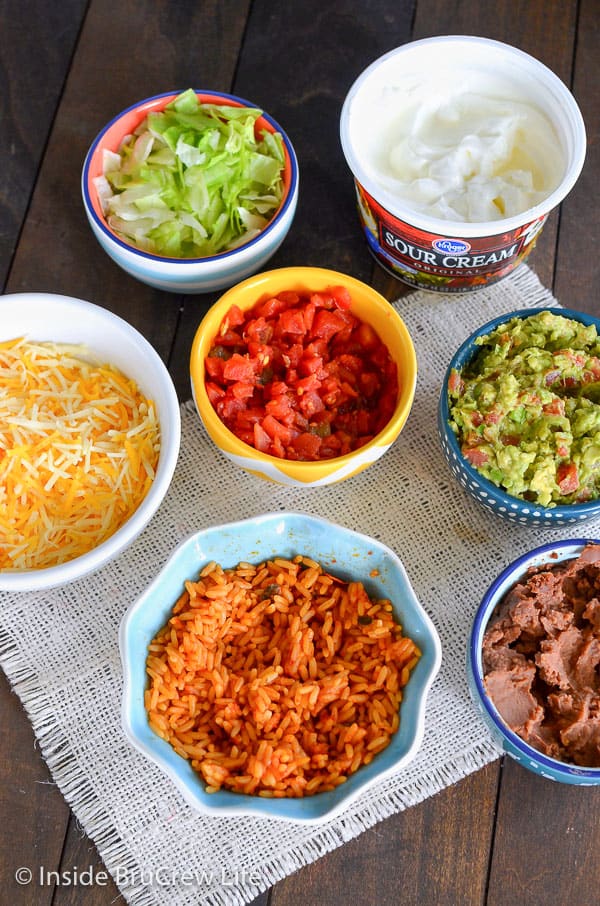 Overhead picture of seven bowls of toppings for seven layer burritos