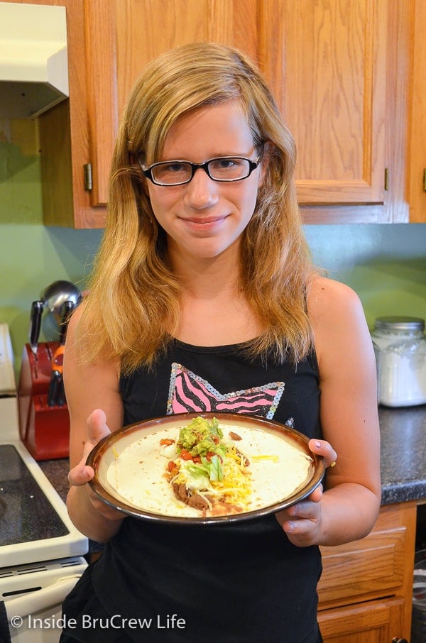 A girl holding a plate with an open face seven layer burrito on it