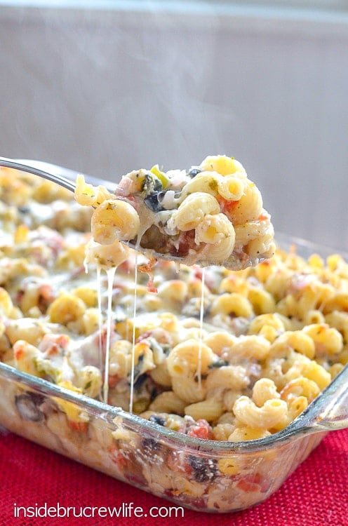 A spoonful of cheesy pasta lifted up from a pan of veggie supreme pasta bake