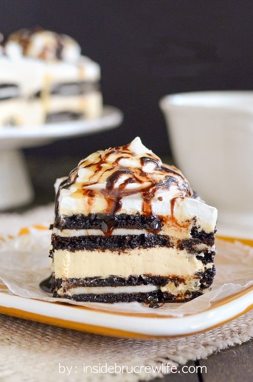 A yellow plate with a piece of salted caramel Oreo icebox cake topped with whipped cream and chocolate syrup on it