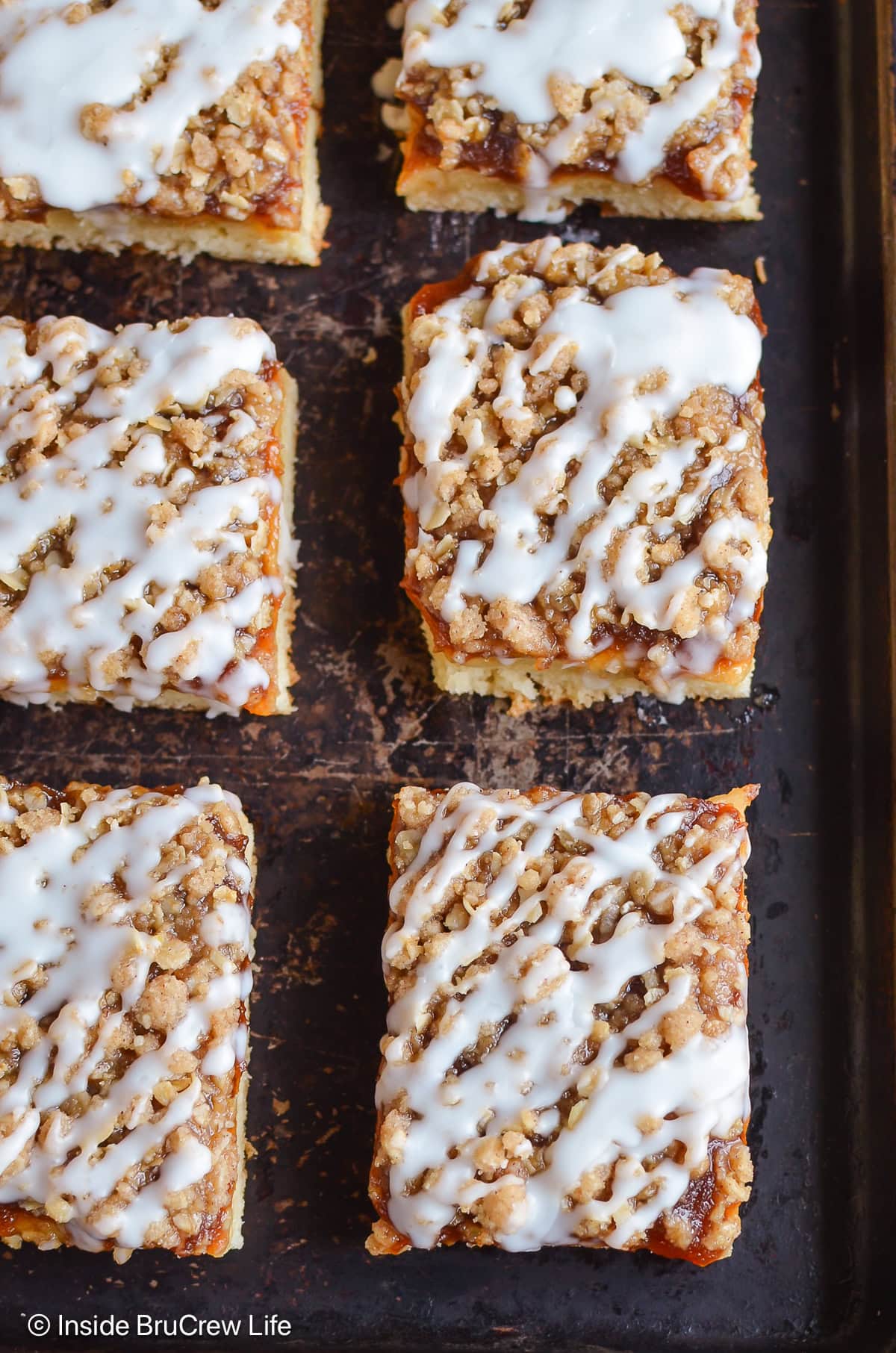 Squares of glazed coffee cake on a dark tray.