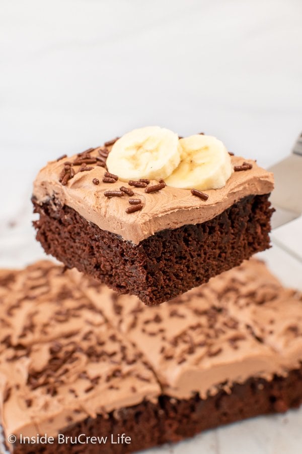 A spatula holding a slice of frosted chocolate banana up in the air.